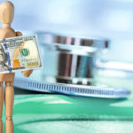 Wooden mannequin holding a US $100 dollar bill on a defocused stethoscope background.